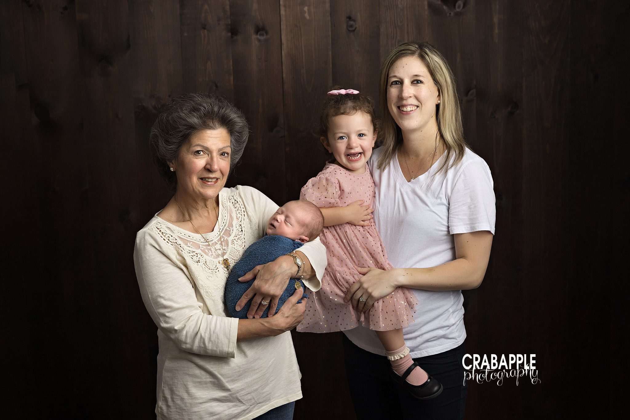 Three generation photo of mom holding toddler daughter and grandmother holding newborn baby boy