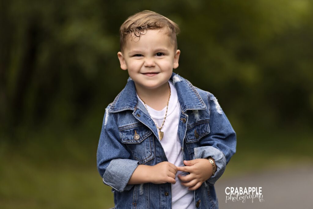 close up of smiling 3 year old boy in denim jacket outdoors during outdoor toddler photos
