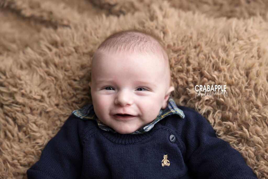 Smiling 3 month old baby boy in navy sweater lying on brown fur blanket
