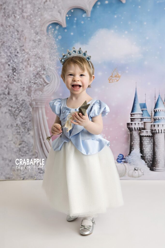 Toddler girl in blue Cinderella dress in front of castle backdrop at Andover MA photography studio
 