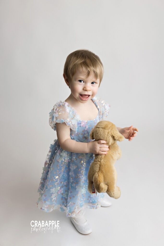 Two year old girl holding stuffed puppy during milestone portrait session