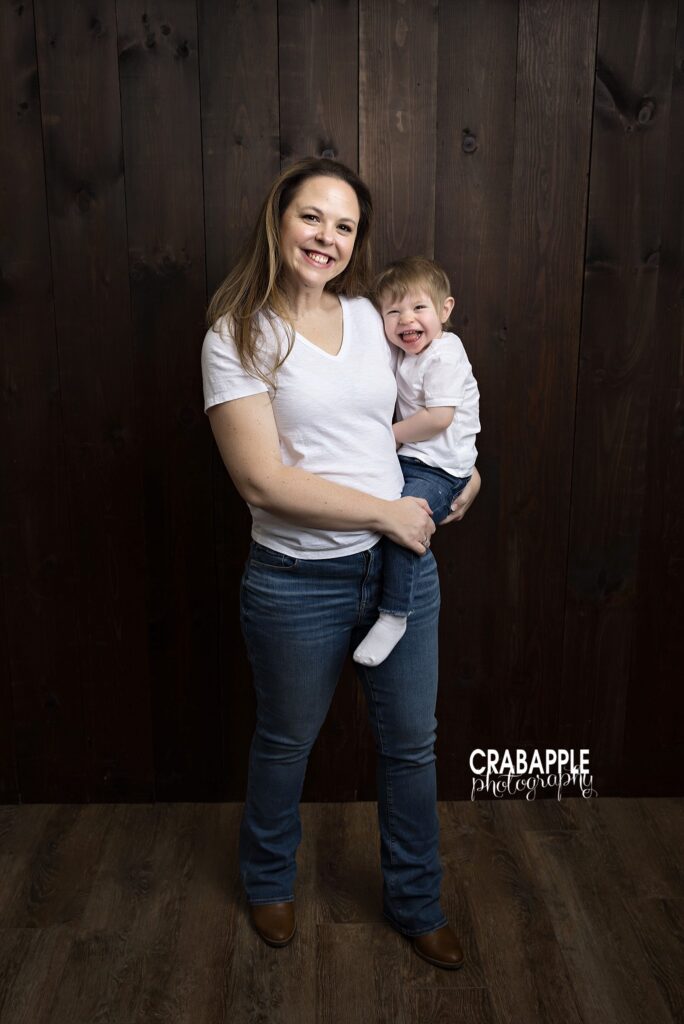 Mother holding toddler daughter in front of dark wood studio backdrop
