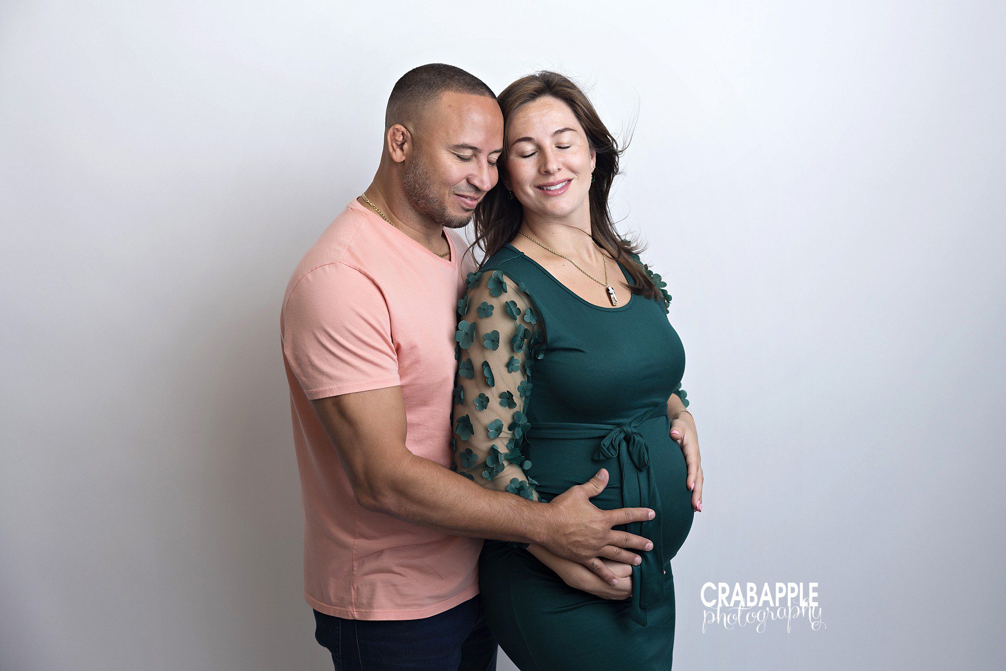 Couple embracing during maternity session with light studio backdrop
