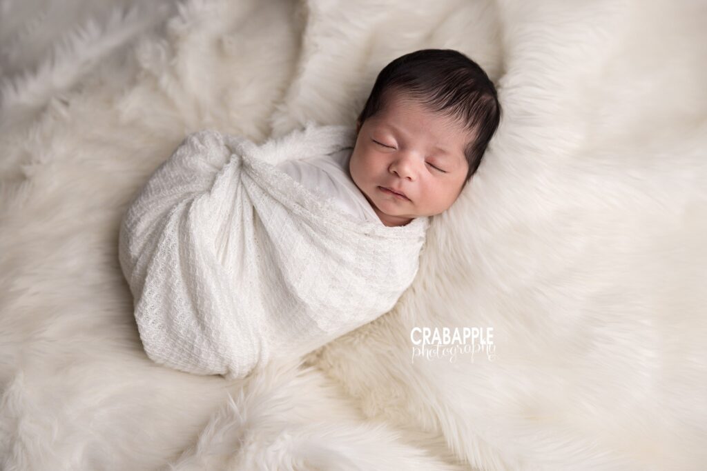 Neutral Newborn Portrait Newborn baby girl wrapped in white swaddle on soft white fur