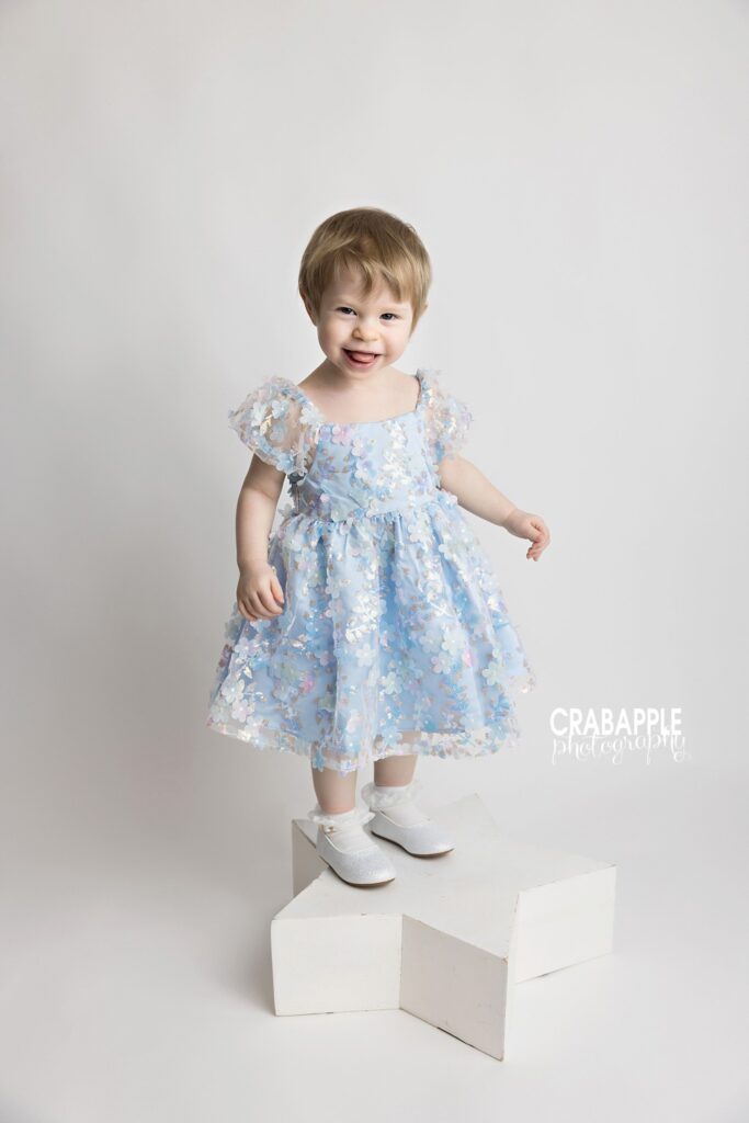 Toddler girl standing on white star box during studio portrait session
