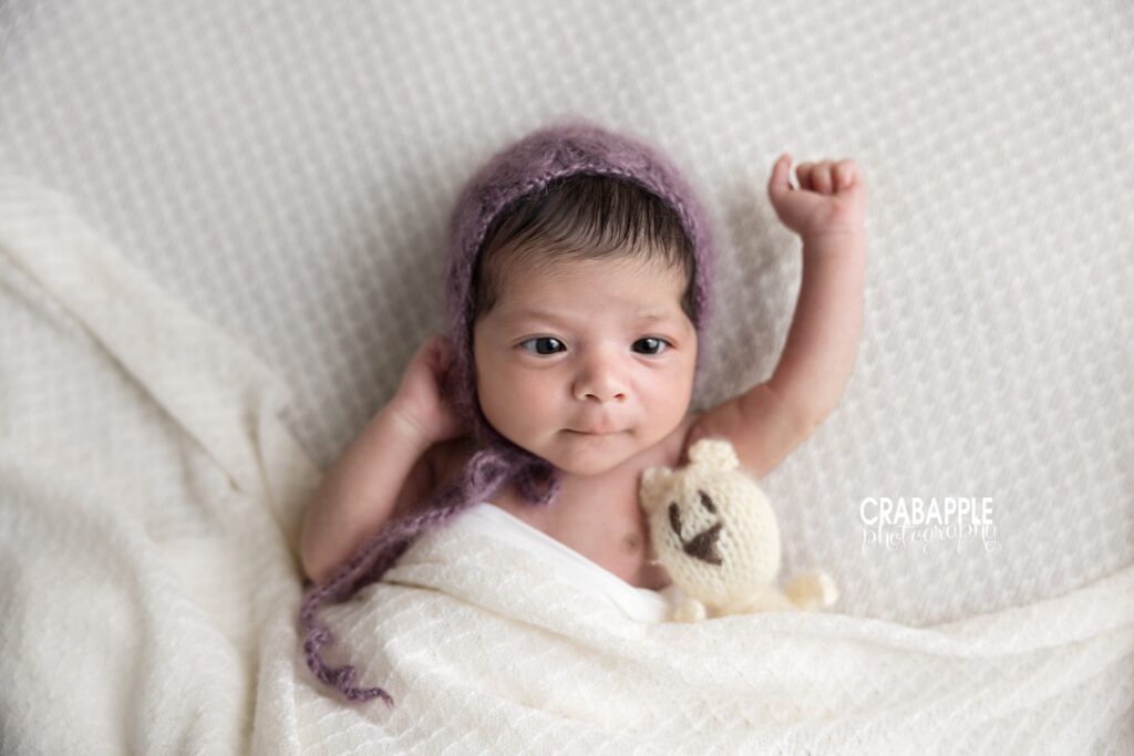 Awake Newborn Stretch Awake newborn baby girl in bonnet beside stuffed animal stretching