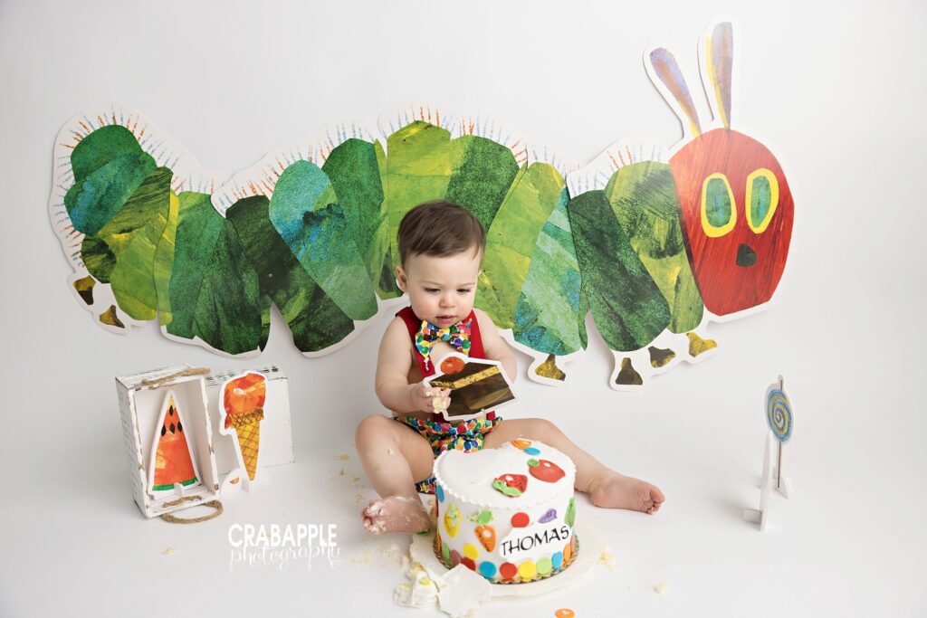 Very Hungry Caterpillar cake smash setup with colorful backdrop and custom birthday cake
