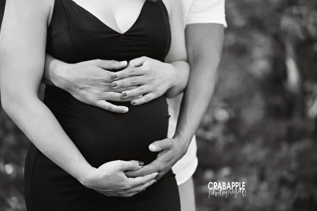 Close up maternity portrait highlighting baby bump with hands outdoors in summer light
