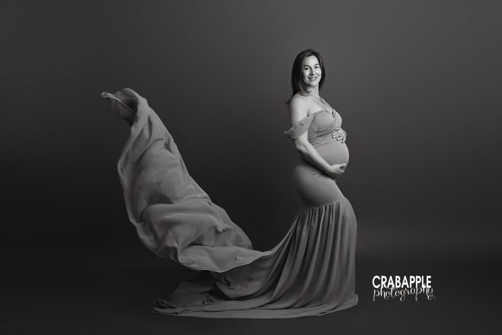 Black and white maternity portrait with flowing gown and dramatic lighting
