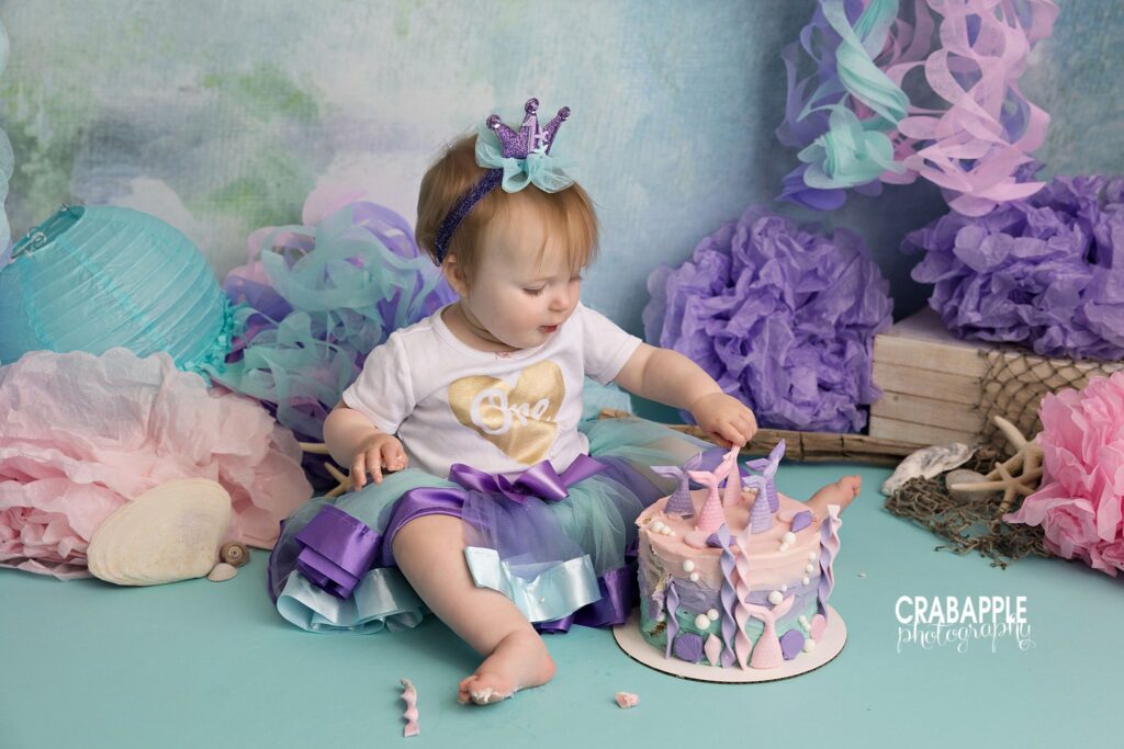 One year old girl enjoying mermaid cake smash setup in studio
