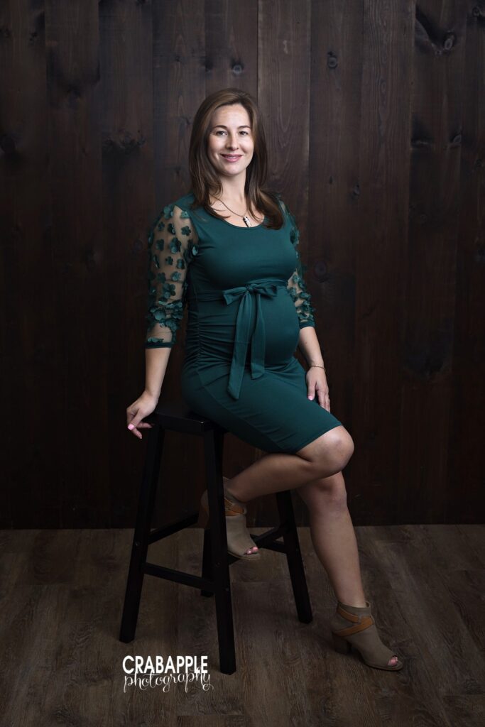 Dramatic maternity portrait with emerald green dress and dark backdrop
