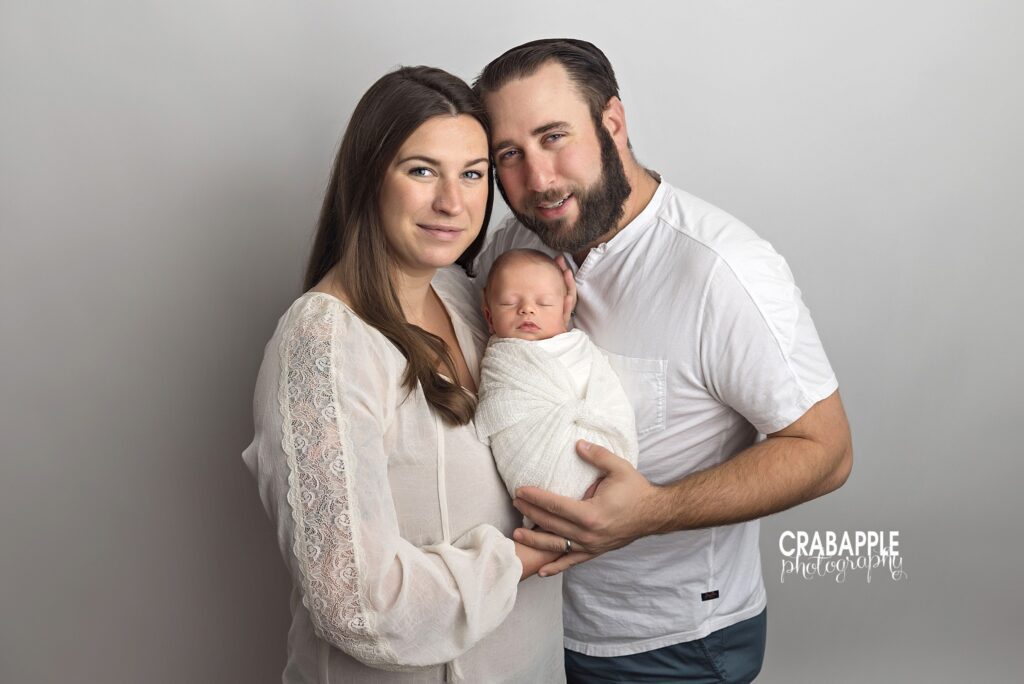 parents holding newborn baby boy in neutral studio portrait
