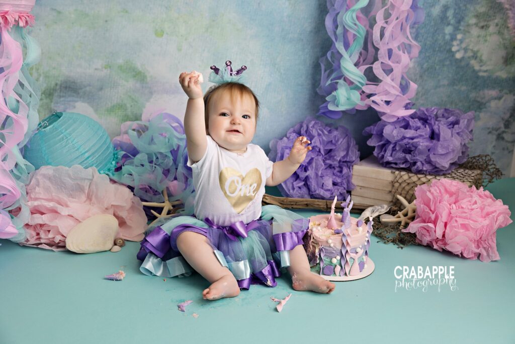 Baby girl sitting with mermaid cake during first birthday photography session
