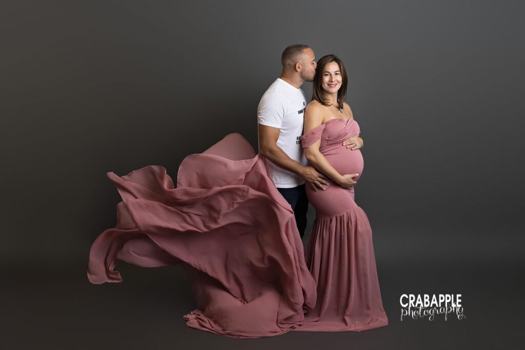 Studio maternity portrait with pink flowing gown and dramatic fabric movement
