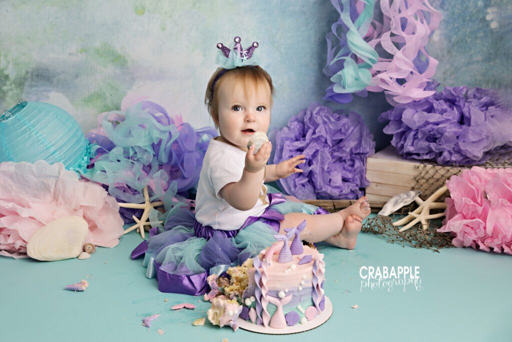 Baby girl exploring mermaid cake during colorful cake smash session
