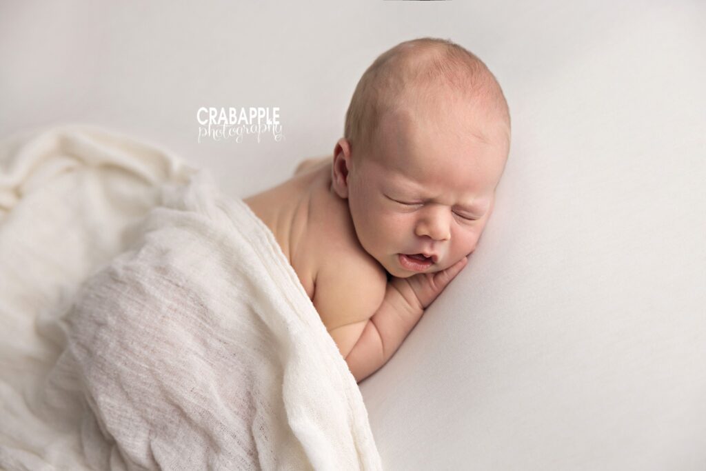 newborn baby boy sleeping with soft white textured blanket
