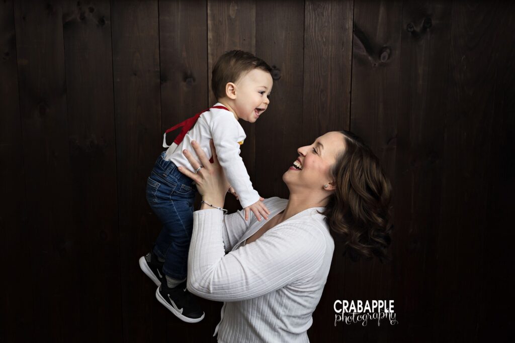 Mom smiling while lifting her one year old son during North Andover family birthday photo session
