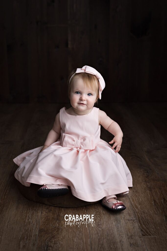 One year old baby girl sitting in pink dress during milestone session
