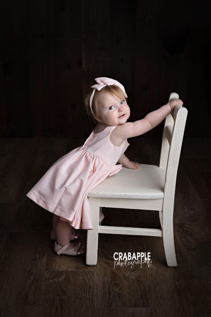 Baby girl standing beside white chair during first birthday photos
