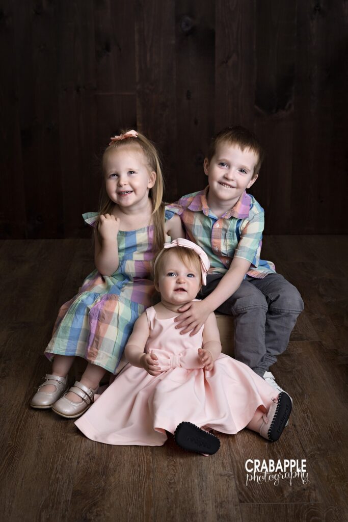 Three siblings sitting together during first birthday family photo session
