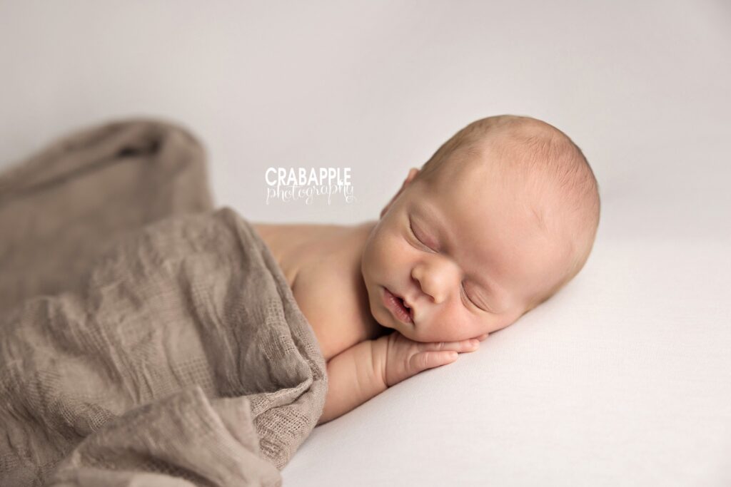 newborn baby boy posed under beige blanket with neutral tones
