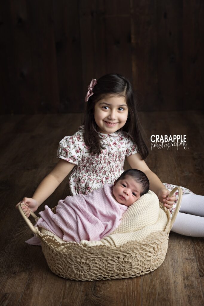 Sister with Newborn Older sister holding newborn baby girl beside basket during newborn session
