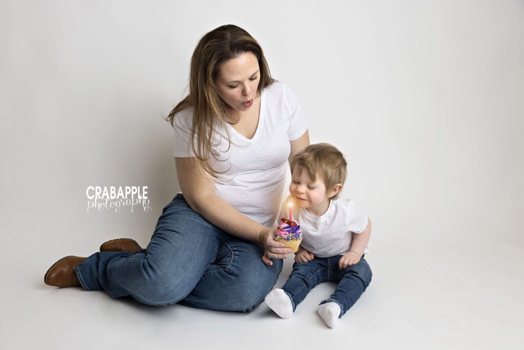 Sweet mommy and me portrait with toddler daughter with birthday cupcake and candle on white backdrop
