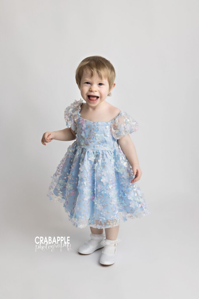 Toddler girl standing and smiling in light blue dress on white backdrop
