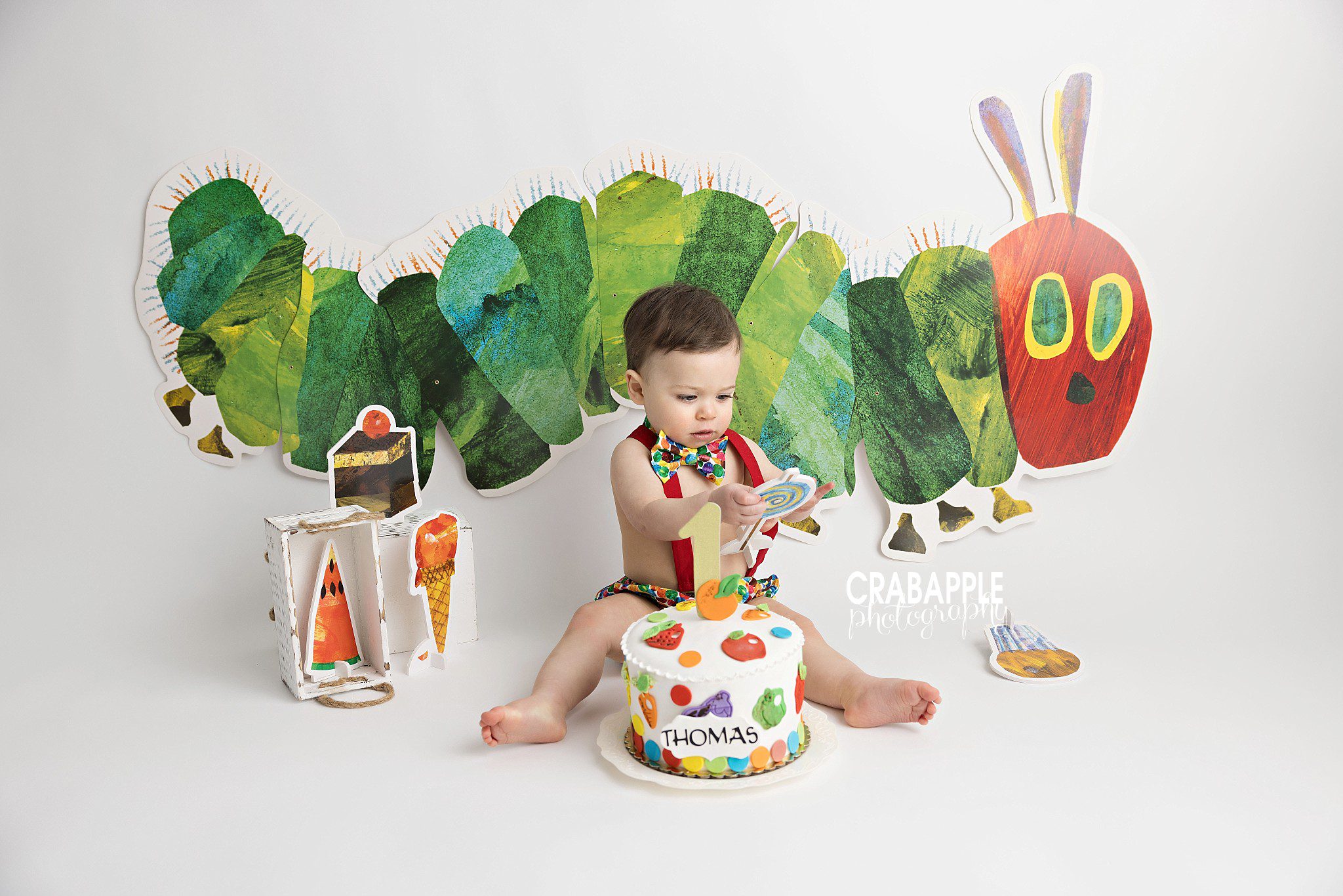 One year old boy sitting in colorful cake smash setup inspired by Eric Carle book
