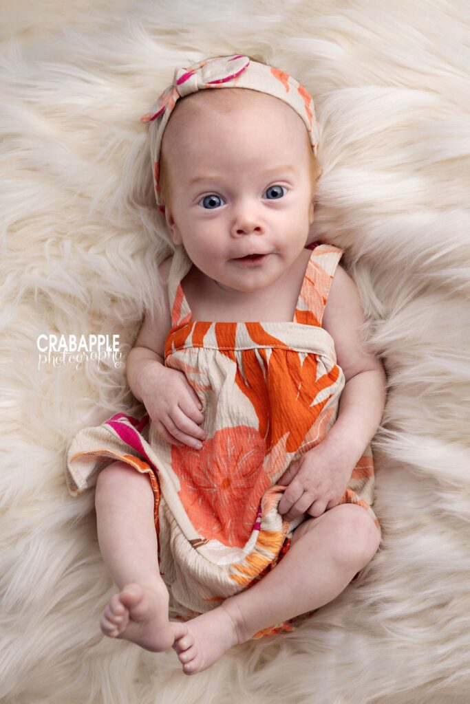 Awake three month old baby girl wearing a pink and orange floral dress

