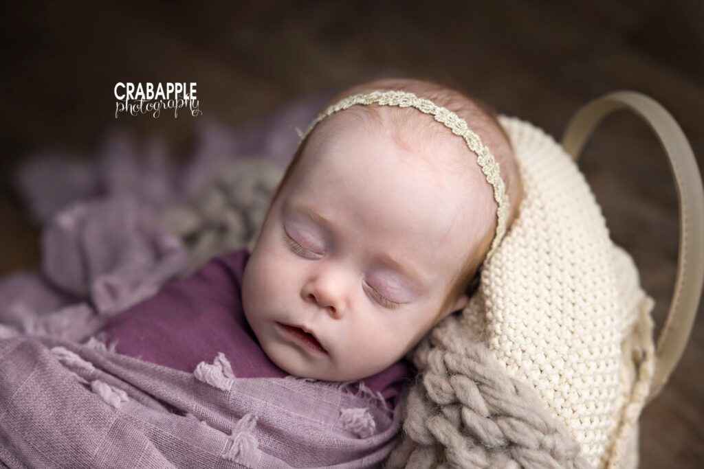 Close-up of baby girl swaddled in basket with textured purple blanket


