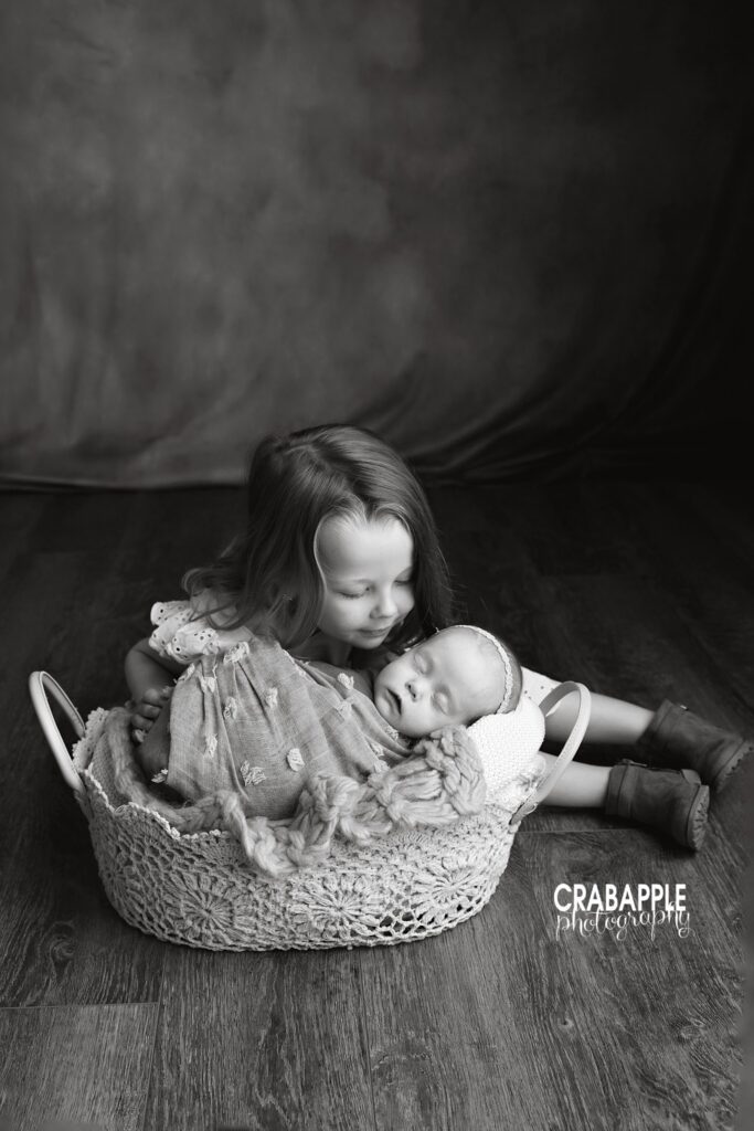 Black and white portrait of big sister kissing her baby sister
