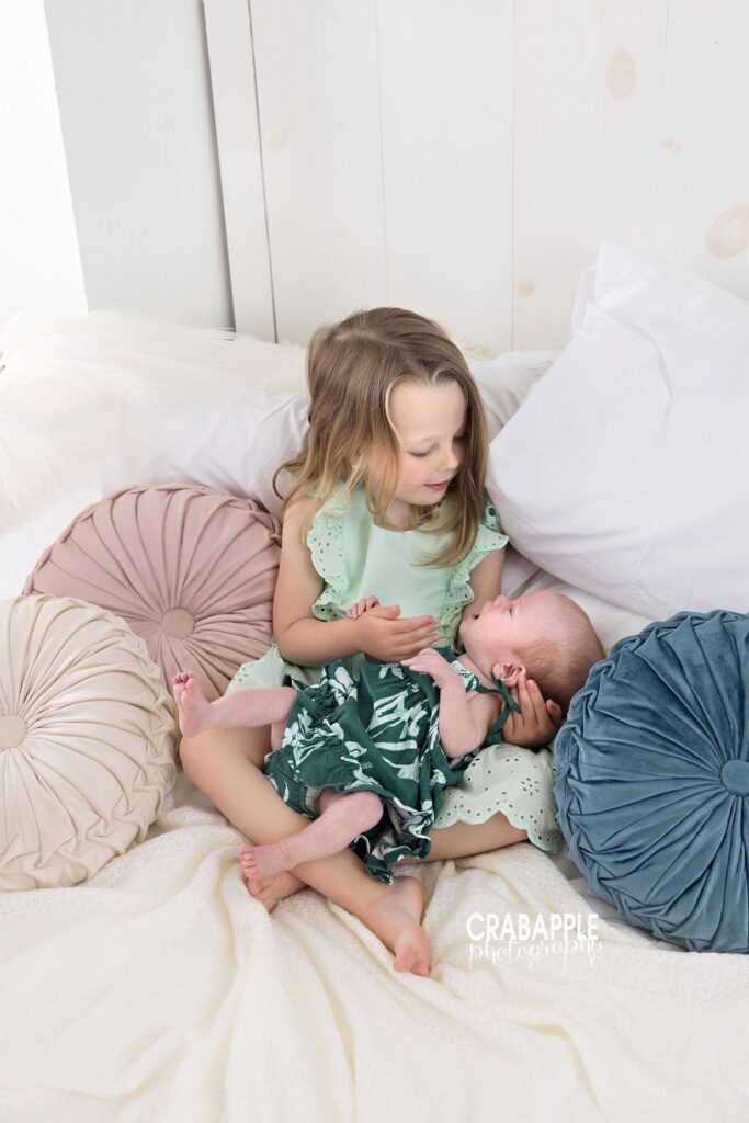 Older sister holding baby sister surrounded by soft pillows
