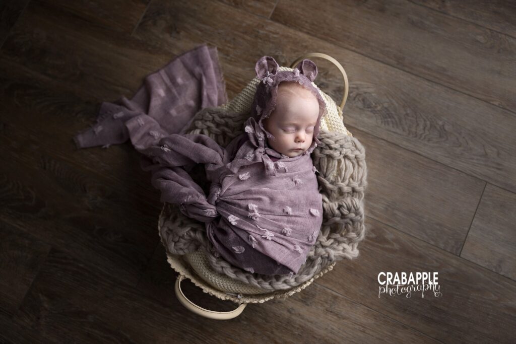 Tiny three month old baby wrapped in purple blanket inside basket

