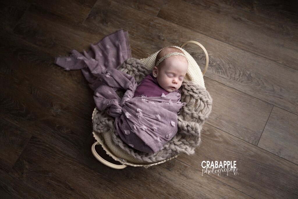 Swaddled baby girl posed in lace basket with purple blanket

