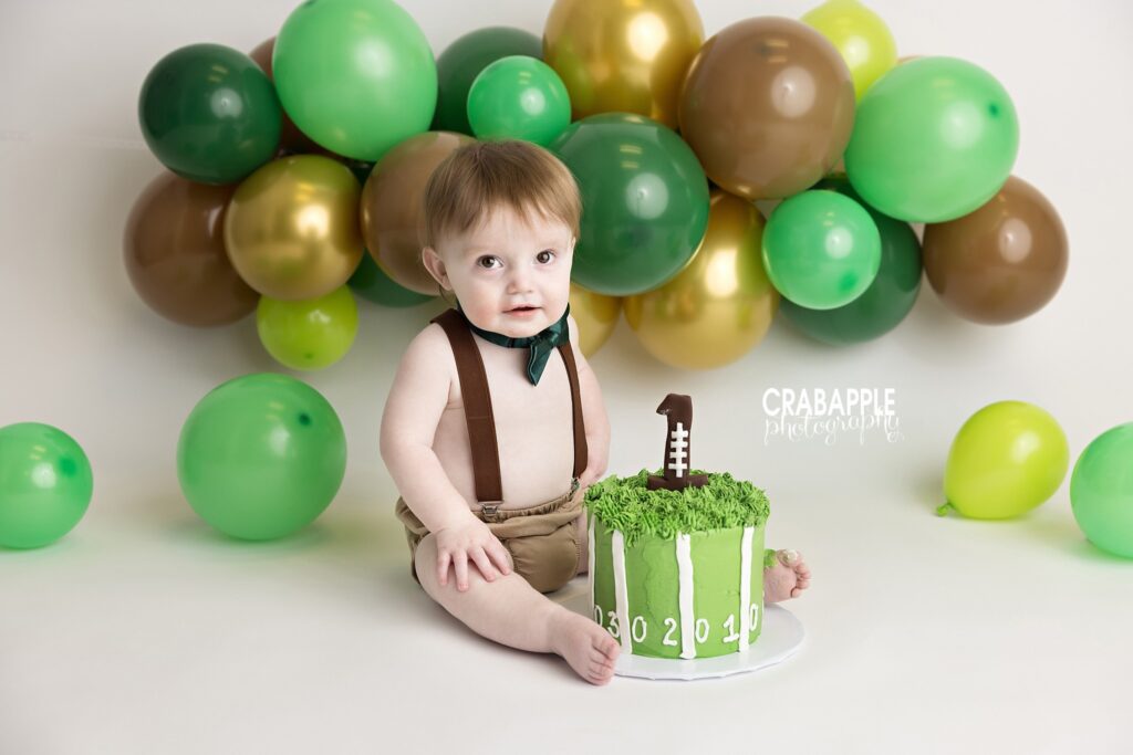 Baby boy first birthday cake smash session with football themed custom setup near Boston MA