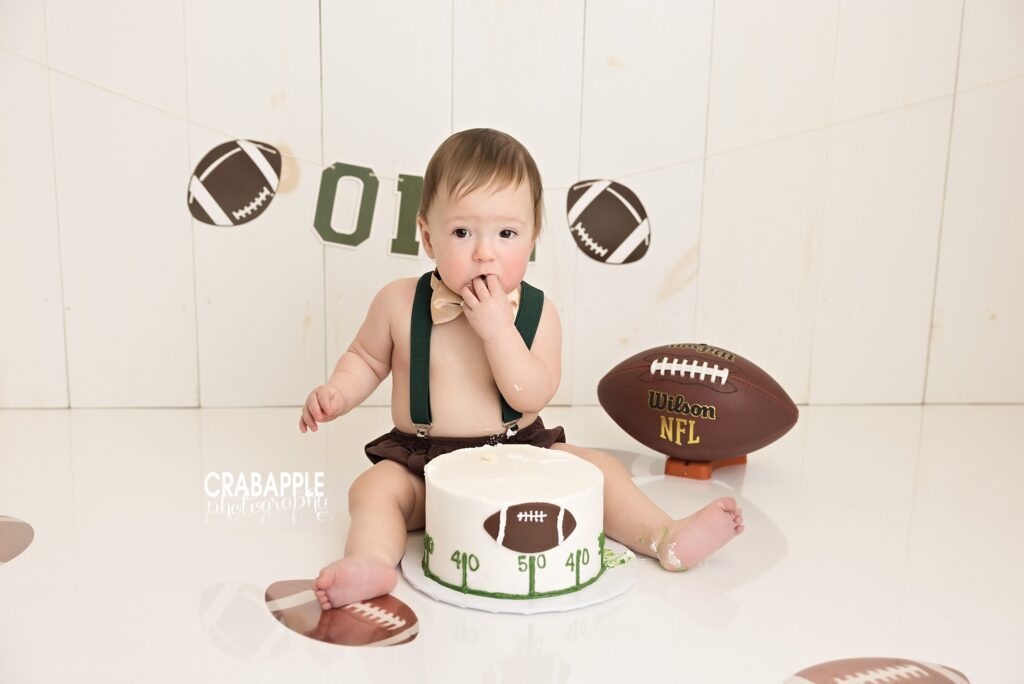 Baby milestone portrait featuring football themed birthday decorations and first birthday cake smash session