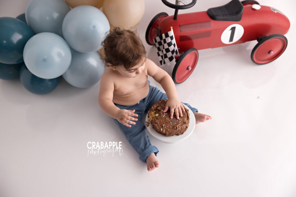 Baby boy celebrating first birthday with race car themed cake smash session in Boston area photography studio