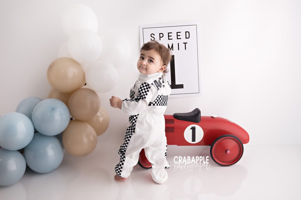 Race car themed cake smash photography session with checkered flag birthday race suit and setup for one year old baby