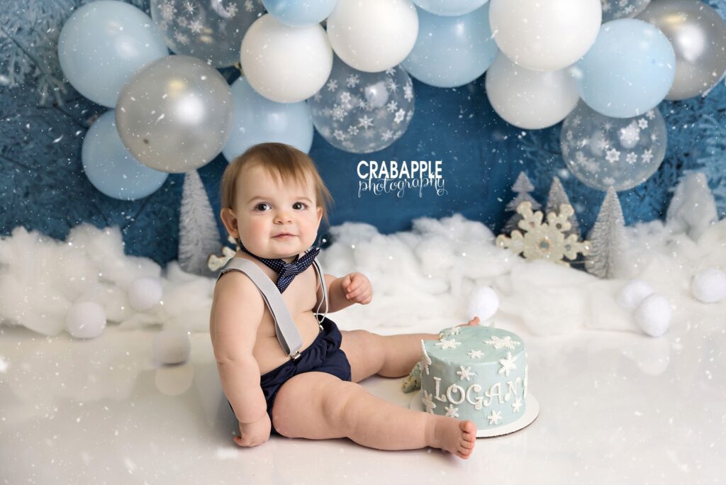 Baby boy enjoying cake smash in winter woodland themed birthday setup
