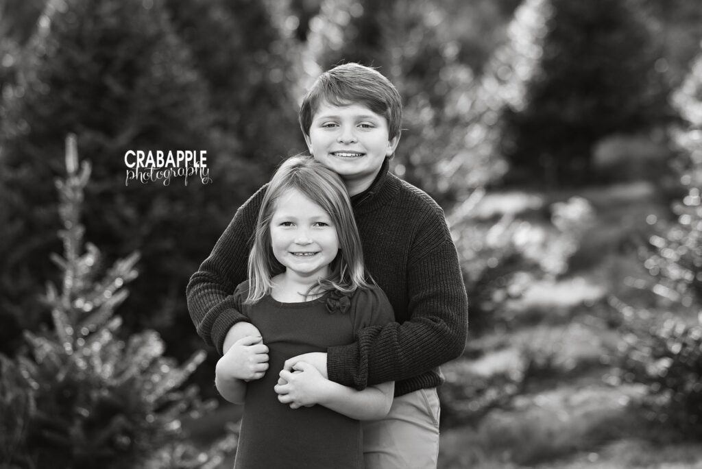 Brother and sister portrait black and white Brother and sister embracing among the evergreen trees in a black and white portrait