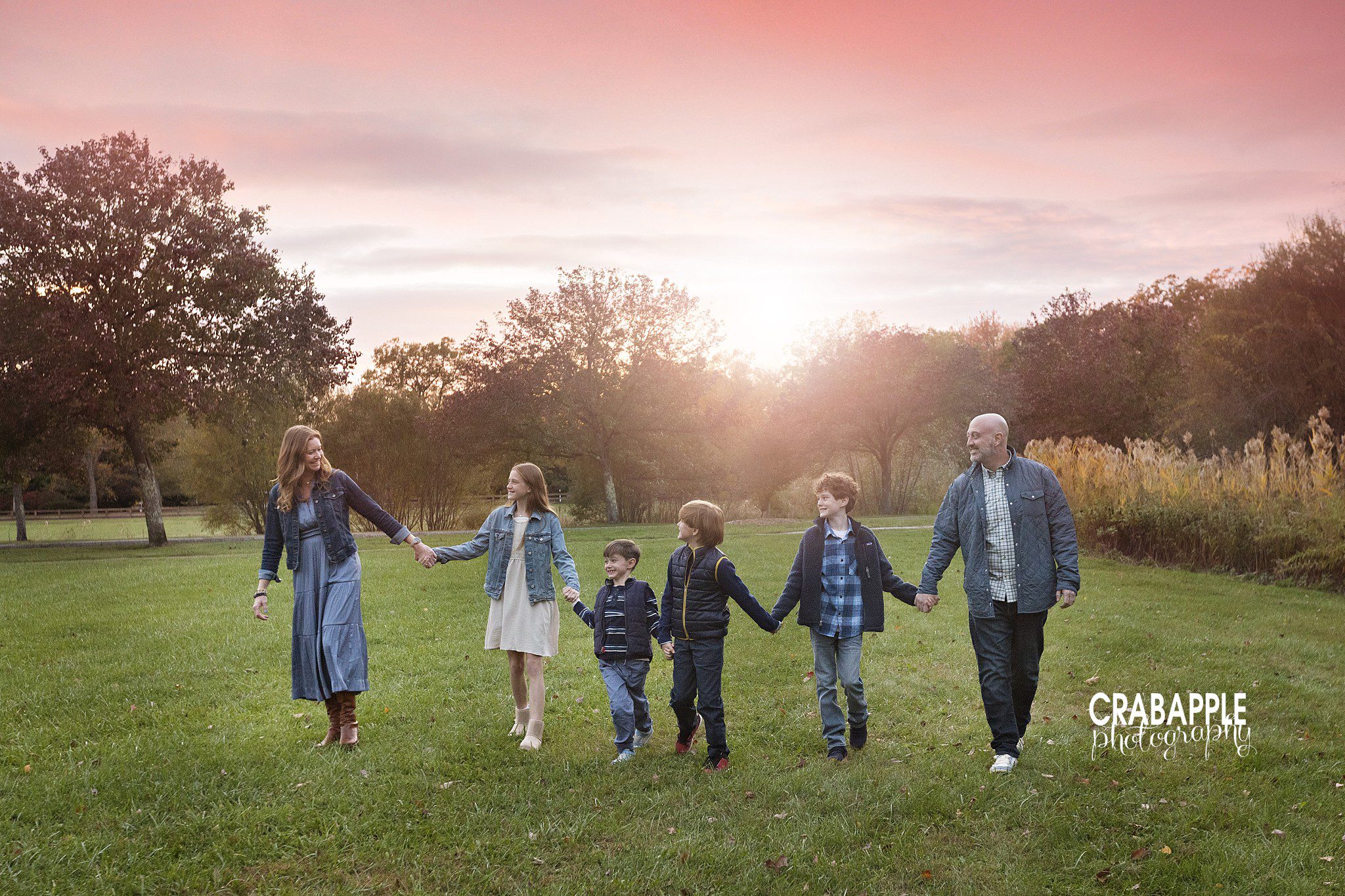Family of six walking hand in hand toward the camera during fall photos at Ipswich River Park
