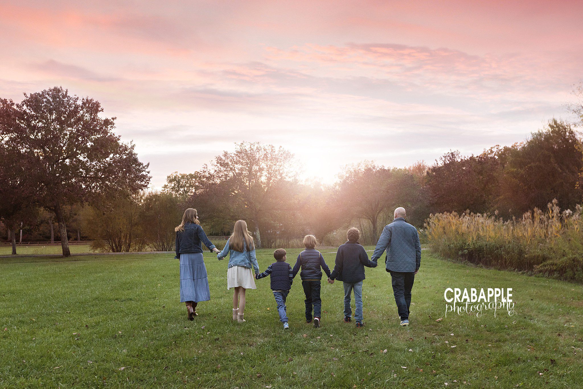 Family walking hand in hand through the field at Ipswich River Park during a fall portrait session
