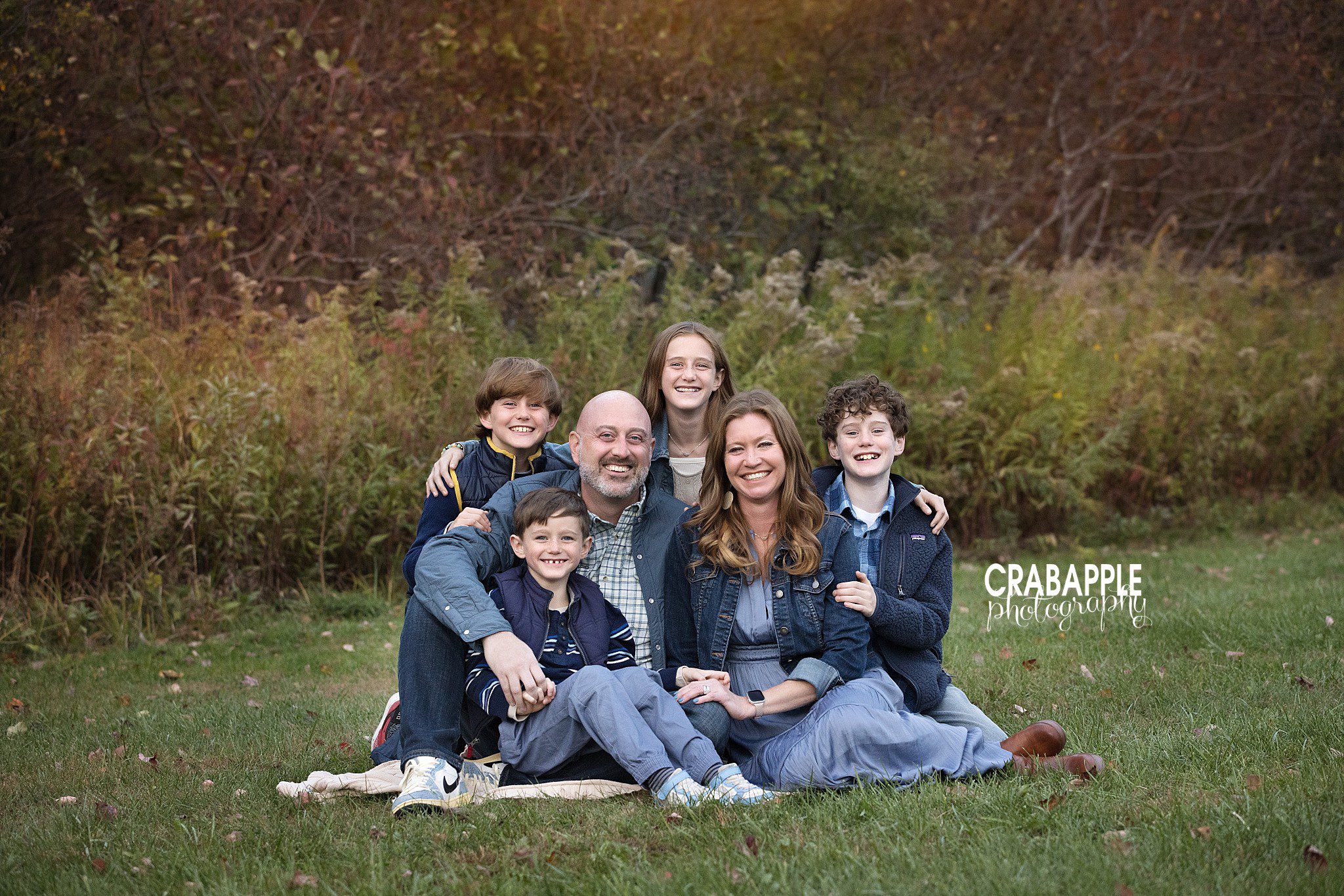Family of six sitting together on a blanket during fall portraits at Ipswich River Park
