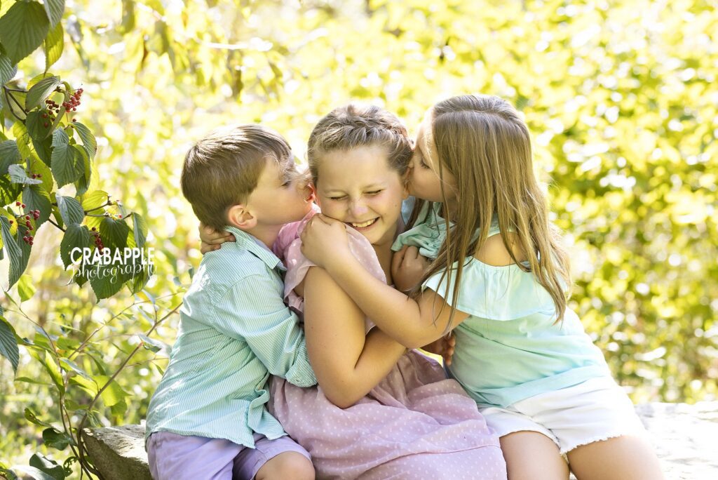 Younger brother and sister kissing their big sister during family portraits
