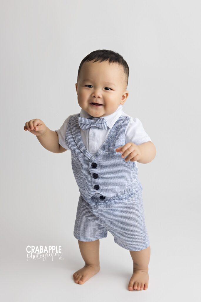 Smiling 10-month-old baby boy standing in a light and airy photography studio