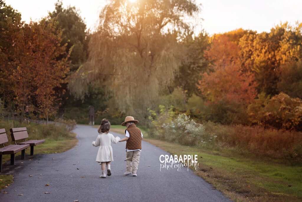 Two toddlers walk hand in hand down an autumn path