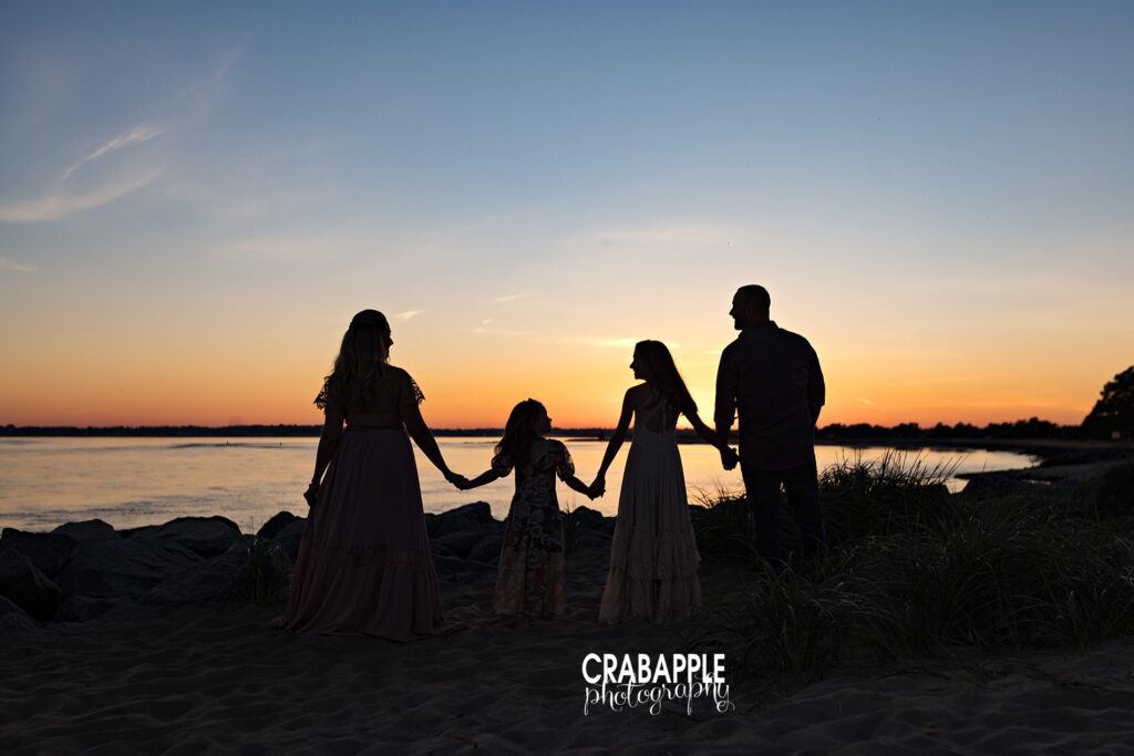 Family of four is silhouetted against the sky by a setting sun with beautiful glow