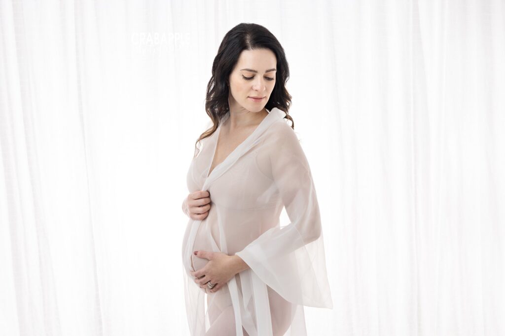 Soft maternity photography portrait Soft maternity portrait of an expecting mother wearing a sheer white robe in the studio