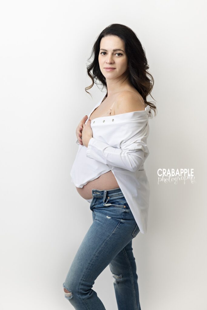 Classic jeans and white shirt maternity portrait Expecting mother in a classic jeans and white shirt maternity outfit against a studio backdrop